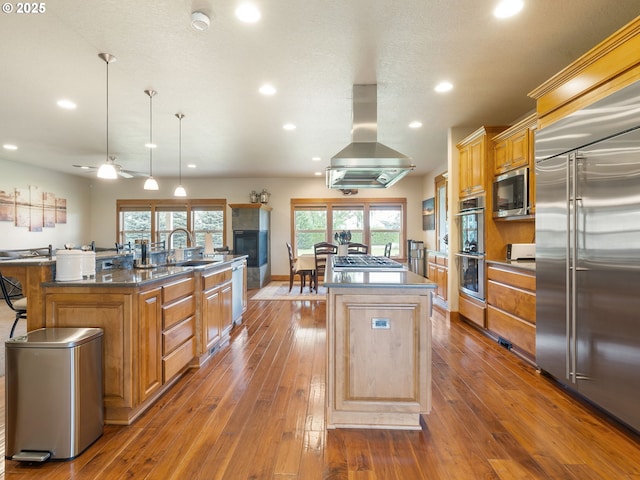 kitchen with a sink, stainless steel appliances, recessed lighting, island range hood, and a center island with sink