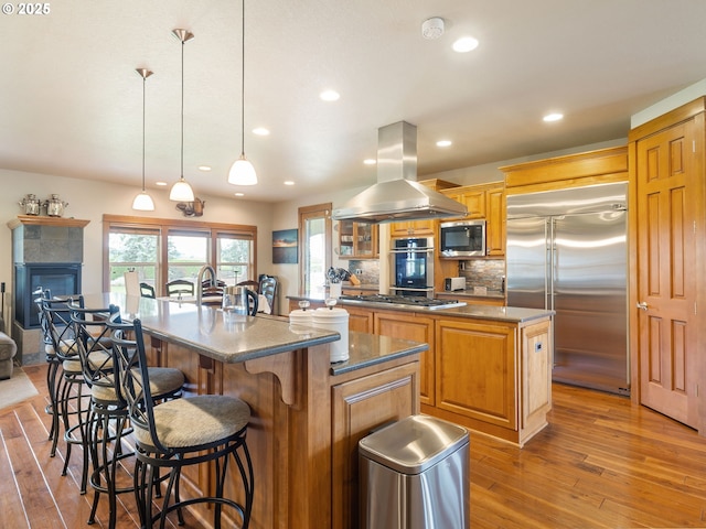kitchen with a large island with sink, wood-type flooring, appliances with stainless steel finishes, and island exhaust hood