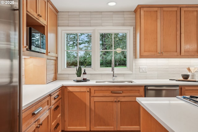 kitchen with appliances with stainless steel finishes, a sink, tasteful backsplash, light countertops, and brown cabinets