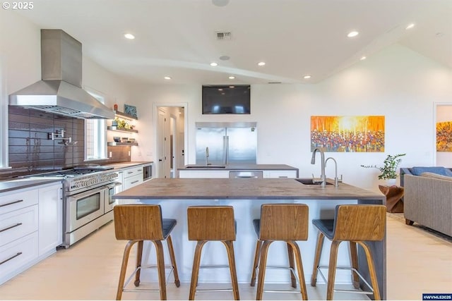 kitchen featuring visible vents, high quality appliances, a center island with sink, a sink, and island range hood