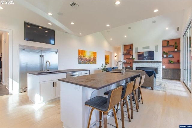 kitchen with dark countertops, visible vents, a center island with sink, and light wood-style floors