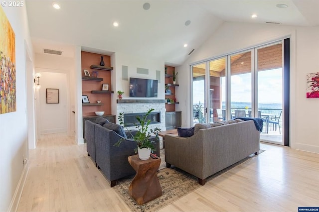 living room with built in features, visible vents, light wood finished floors, a stone fireplace, and vaulted ceiling