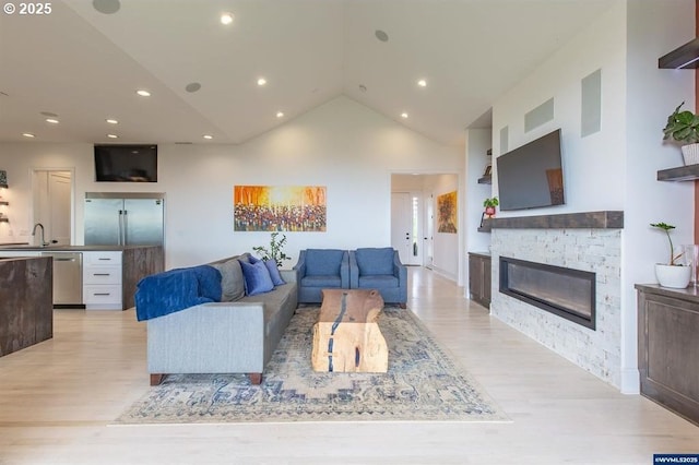 living room with a glass covered fireplace, light wood-style flooring, visible vents, and high vaulted ceiling