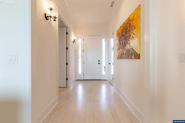 hallway with visible vents, light wood-style flooring, baseboards, and ornamental molding