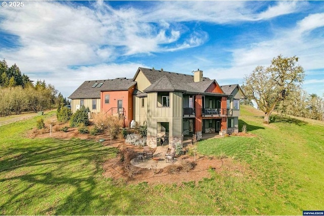 rear view of property with board and batten siding, a lawn, a chimney, a patio area, and stone siding