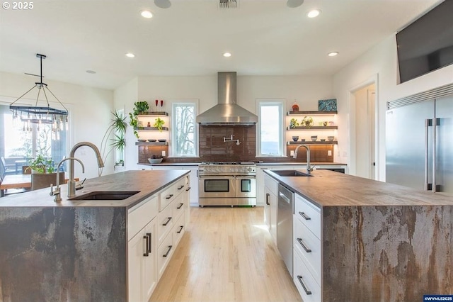 kitchen featuring stainless steel appliances, an island with sink, wall chimney range hood, and open shelves