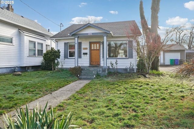 bungalow with a shingled roof, an outbuilding, a detached garage, and a front lawn