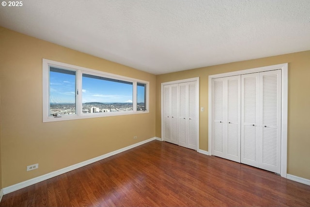 unfurnished bedroom featuring hardwood / wood-style floors, multiple closets, and a textured ceiling