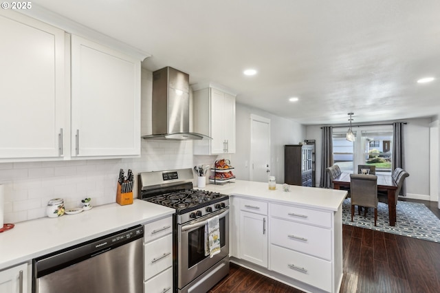 kitchen featuring dark wood-style floors, a peninsula, appliances with stainless steel finishes, and wall chimney exhaust hood