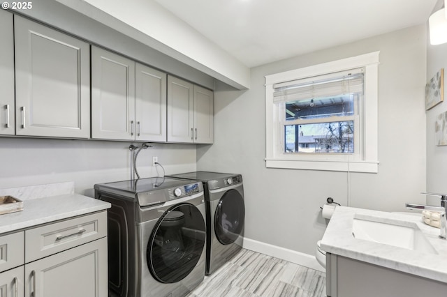 washroom with a sink, cabinet space, baseboards, and washer and clothes dryer