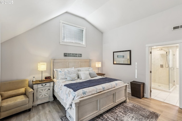 bedroom featuring light wood-type flooring, visible vents, ensuite bath, and vaulted ceiling