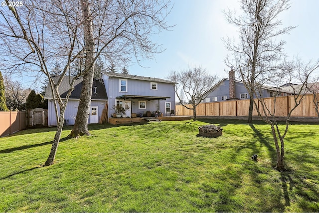 back of property with a wooden deck, a yard, a fenced backyard, and a fire pit