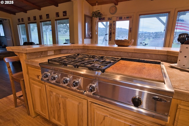 kitchen with tile countertops, vaulted ceiling with beams, a healthy amount of sunlight, and light wood-style floors