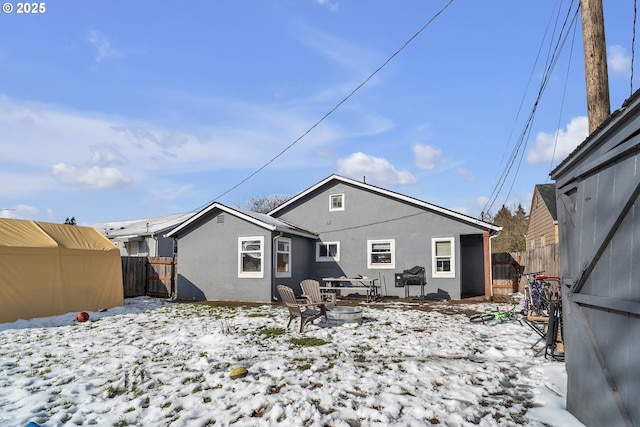 snow covered back of property featuring an outdoor fire pit, fence, and stucco siding