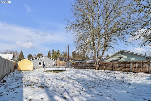 snow covered property featuring a trampoline, an outbuilding, a fenced backyard, and a storage shed