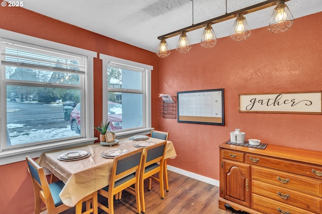 dining room featuring a textured ceiling, a textured wall, dark wood finished floors, and baseboards