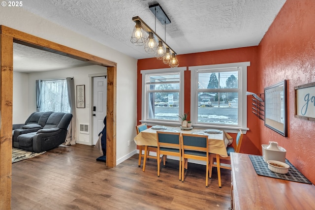 dining space featuring a textured wall, wood finished floors, visible vents, and baseboards