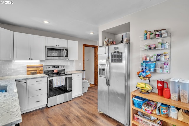 kitchen featuring tasteful backsplash, white cabinets, appliances with stainless steel finishes, wood finished floors, and light stone countertops