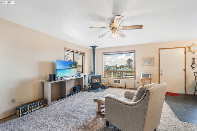 living room featuring a wall unit AC, visible vents, a wood stove, ceiling fan, and carpet flooring