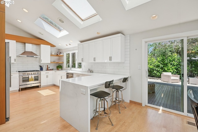 8895 SW Bohmann Pkwy, Portland, OR 97223 - kitchen with appliances with stainless steel finishes, wall chimney exhaust hood, a skylight, a peninsula, and decorative backsplash