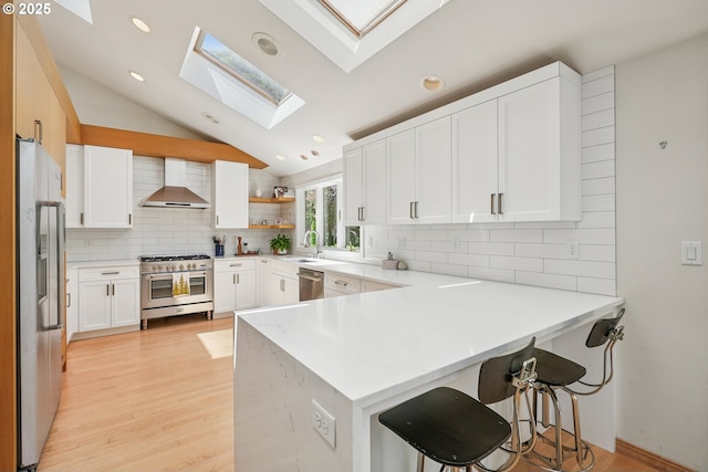 8895 SW Bohmann Pkwy, Portland, OR 97223 - kitchen with stainless steel appliances, wall chimney exhaust hood, a skylight, a peninsula, and a sink