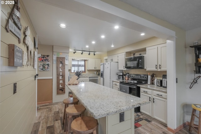 kitchen featuring black appliances, a breakfast bar, a center island, light stone countertops, and white cabinets