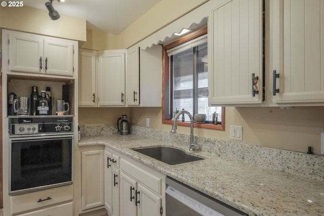 kitchen featuring black oven, a sink, dishwasher, light stone counters, and white cabinetry