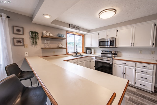 3308 Honeywood St, Eugene, OR 97408 - kitchen featuring appliances with stainless steel finishes, a sink, white cabinetry, light countertops, and a peninsula