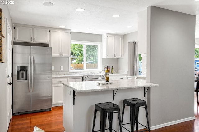 4782 Lowell Ave, Keizer, OR 97303 - kitchen with stainless steel refrigerator with ice dispenser, a kitchen bar, wood finished floors, white cabinetry, and light stone countertops