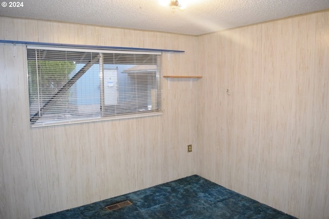 unfurnished room featuring wooden walls, a textured ceiling, visible vents, and dark carpet