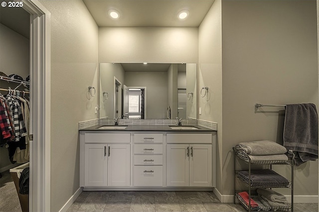 full bath with double vanity, a sink, a walk in closet, and baseboards