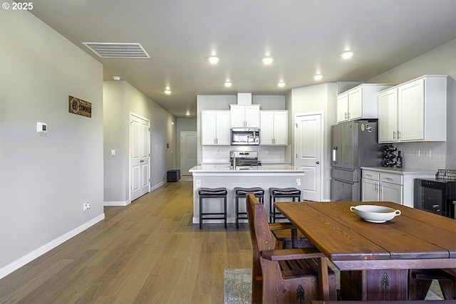 kitchen featuring visible vents, an island with sink, stainless steel appliances, light countertops, and light wood-style floors