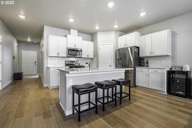 kitchen with beverage cooler, a breakfast bar area, appliances with stainless steel finishes, wood finished floors, and light countertops