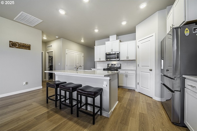 kitchen featuring wood finished floors, a sink, visible vents, appliances with stainless steel finishes, and tasteful backsplash