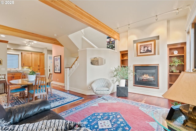 living area with rail lighting, wood finished floors, stairway, baseboards, and a glass covered fireplace