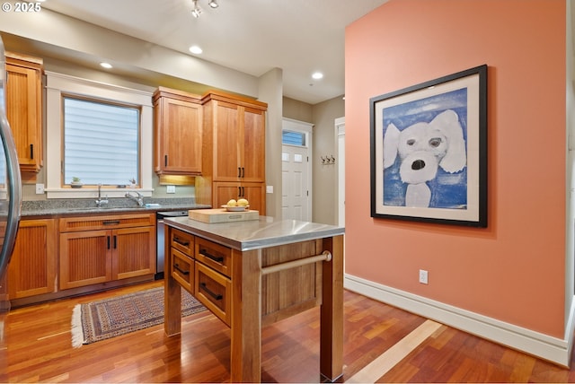 kitchen with brown cabinets, a sink, light wood-style floors, baseboards, and stainless steel dishwasher