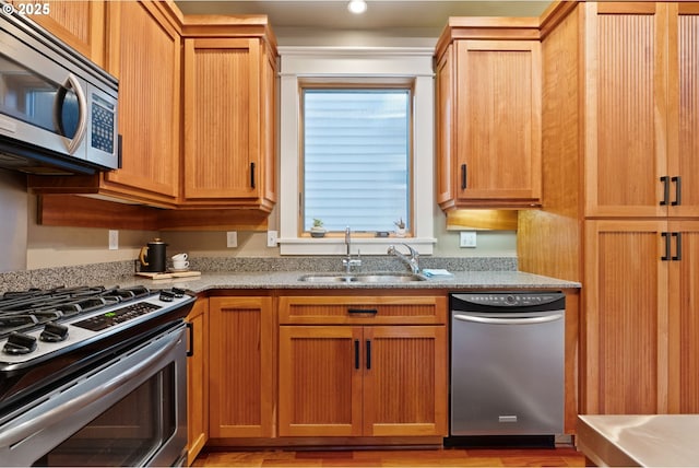kitchen featuring light stone counters, a sink, appliances with stainless steel finishes, and light wood-type flooring