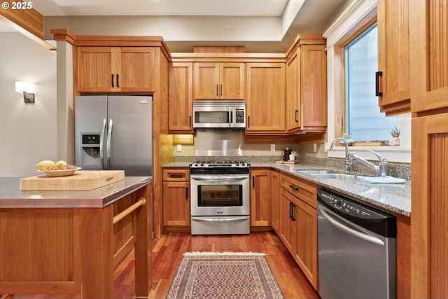 kitchen with a sink, appliances with stainless steel finishes, wood finished floors, and light stone countertops