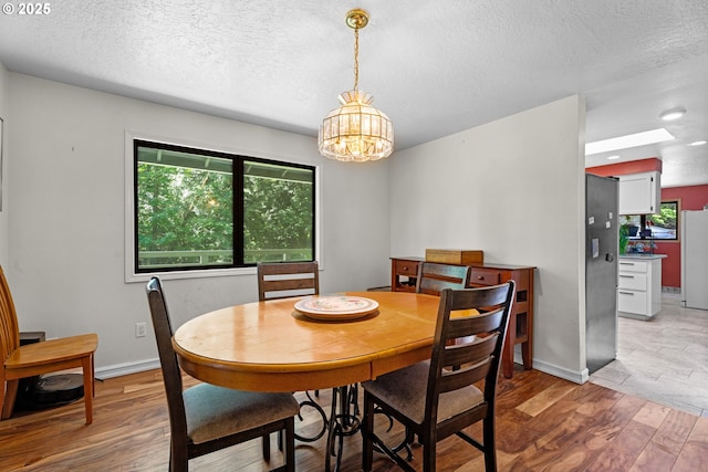 dining space with wood finished floors, a chandelier, a textured ceiling, and baseboards