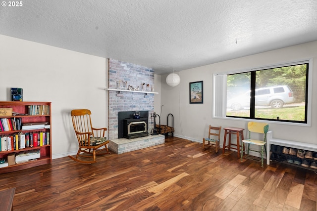 sitting room featuring a textured ceiling, wood finished floors, a wood stove, and baseboards