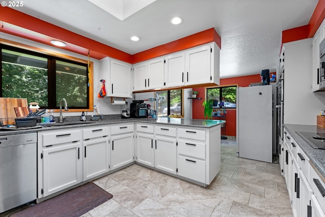 kitchen featuring stainless steel dishwasher, freestanding refrigerator, a sink, white cabinetry, and a peninsula
