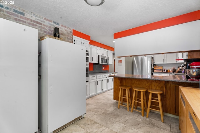 kitchen with stainless steel appliances, white cabinets, dark countertops, a peninsula, and a textured ceiling