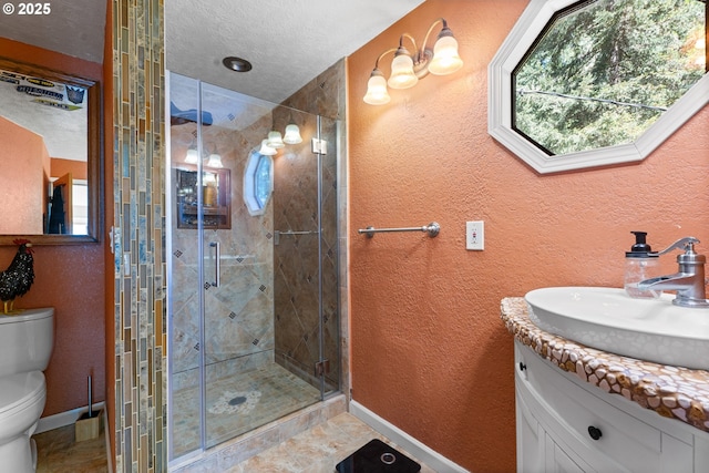 bathroom featuring a shower stall, toilet, vanity, baseboards, and a textured wall