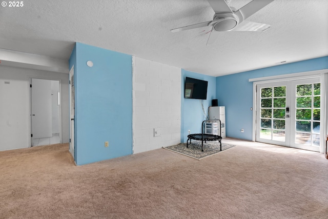 unfurnished room featuring carpet flooring, a textured ceiling, a ceiling fan, french doors, and concrete block wall