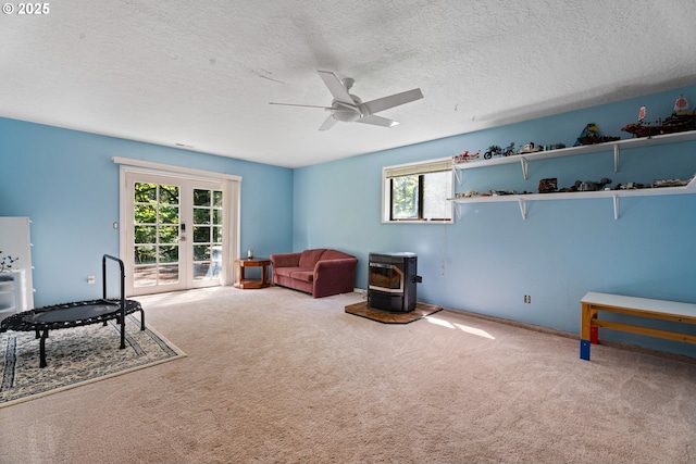 sitting room with a wood stove, ceiling fan, carpet flooring, a textured ceiling, and french doors