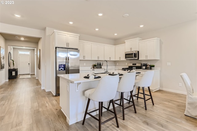 kitchen with recessed lighting, light wood-style floors, a breakfast bar area, white cabinets, and appliances with stainless steel finishes