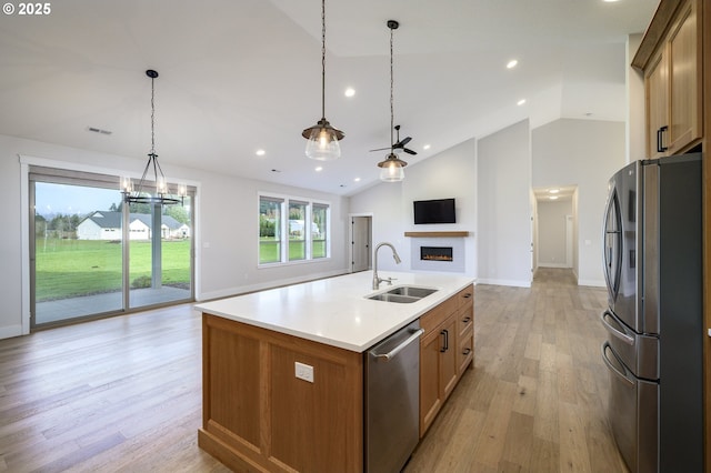 kitchen with sink, hanging light fixtures, a kitchen island with sink, appliances with stainless steel finishes, and light wood-type flooring