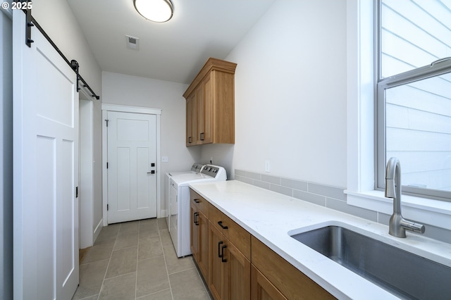 washroom featuring cabinets, washing machine and clothes dryer, sink, light tile patterned flooring, and a barn door