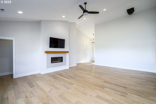 unfurnished living room with vaulted ceiling, a brick fireplace, light hardwood / wood-style floors, and ceiling fan