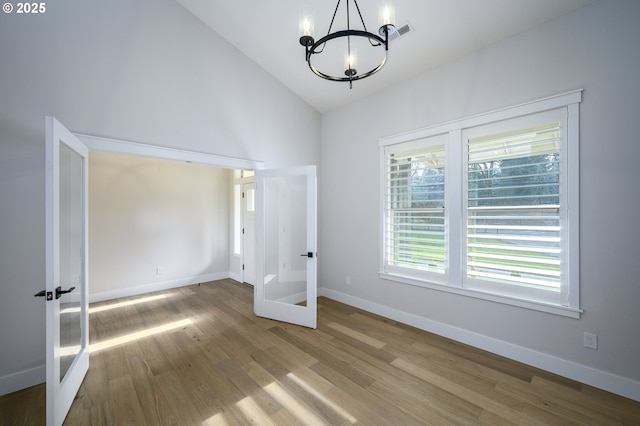 unfurnished bedroom with high vaulted ceiling, french doors, a notable chandelier, and hardwood / wood-style floors